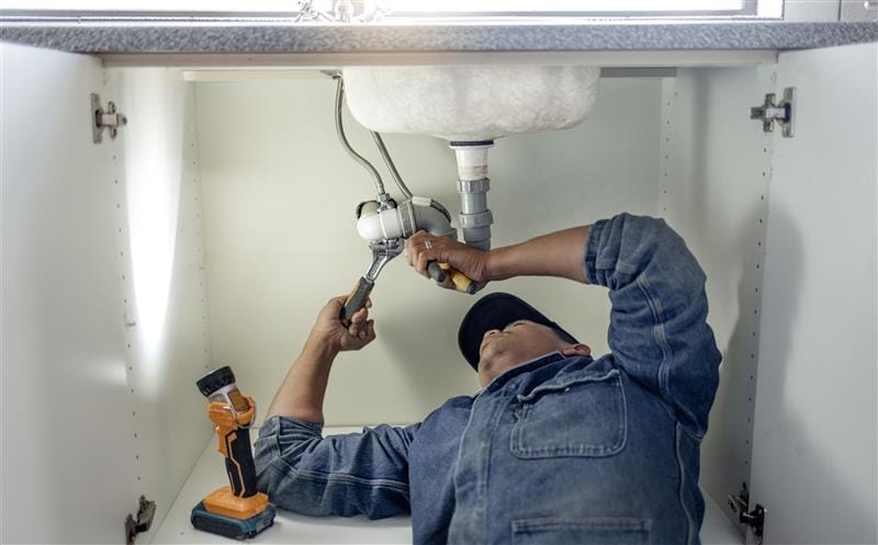 Plumber repairing pipes beneath a bathroom sink in DeBary