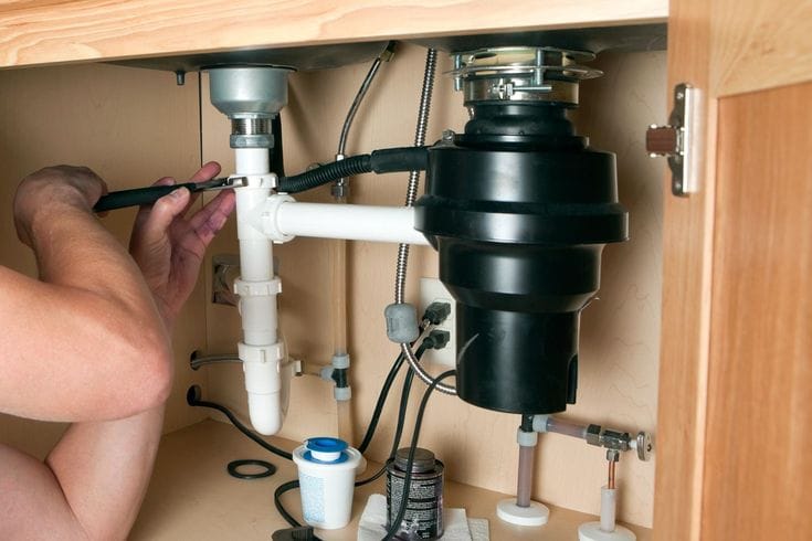 Plumber installing a garbage disposal beneath a kitchen sink in DeBary