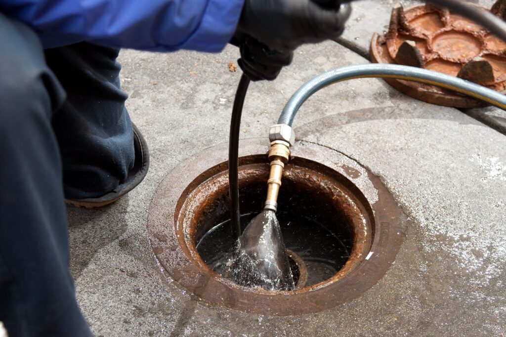Plumber hydro jetting a sewer line through a manhole in DeBary