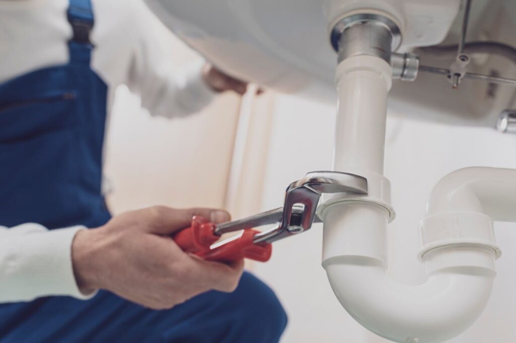 Plumber repairing a white drain pipe beneath a sink in DeBary