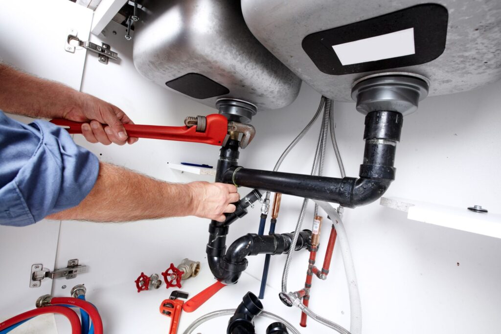 Plumber repairing drain pipes beneath a kitchen sink in DeBary